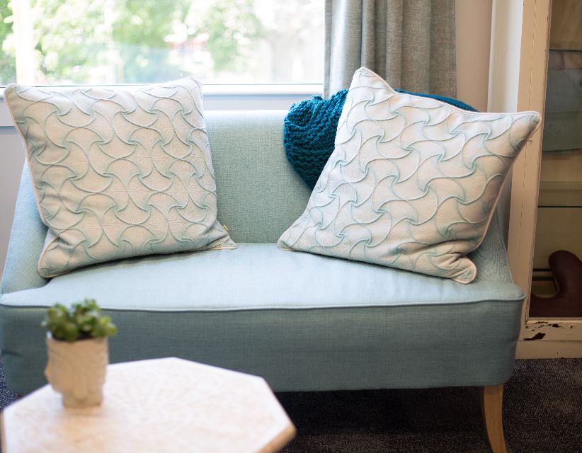A therapy room with a soft green sofa and cushions beside a window